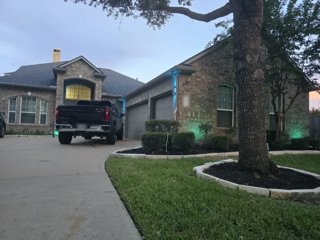 Teal Color-Changing Landscape Lighting – Houston - Laymance Lighting Houston brick home at dusk with teal color-changing uplights on the walls and garage columns, controlled from a phone app, by Laymance Lighting