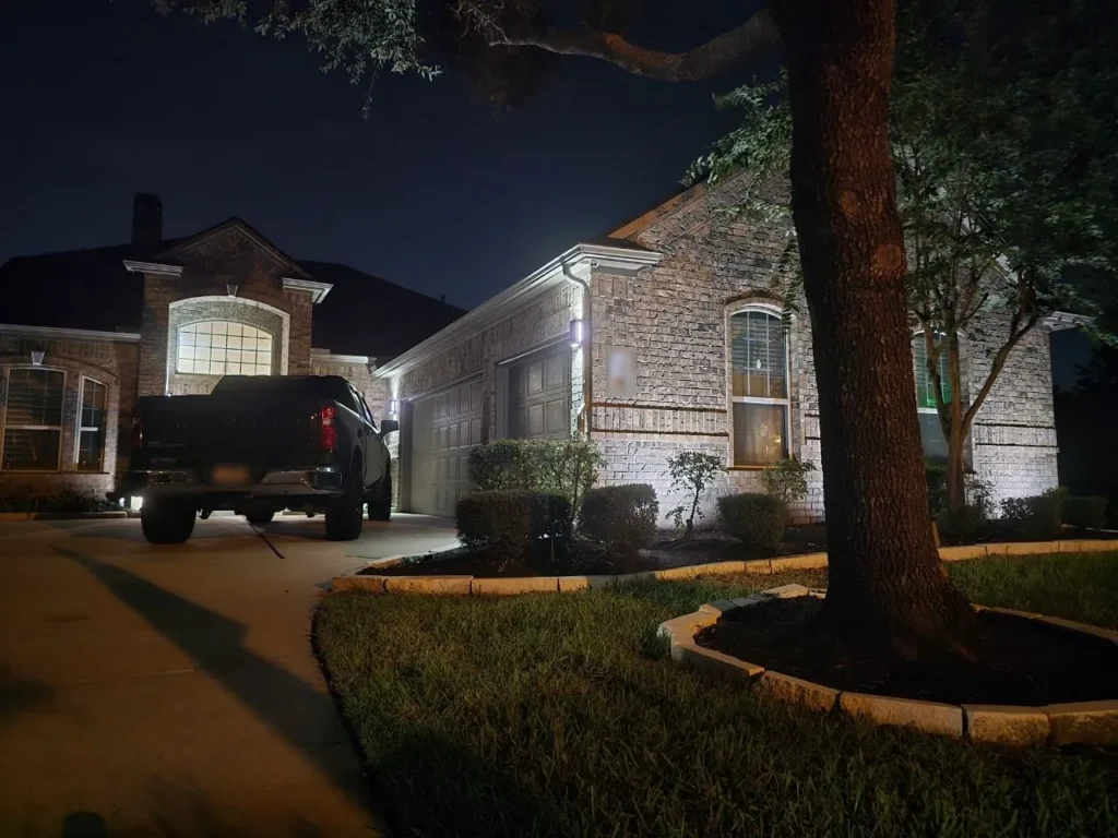 White Landscape Uplighting at Night – Houston - Laymance Lighting Houston brick home at night with bright white landscape uplighting on the facade, garage columns, and entry, by Laymance Lighting